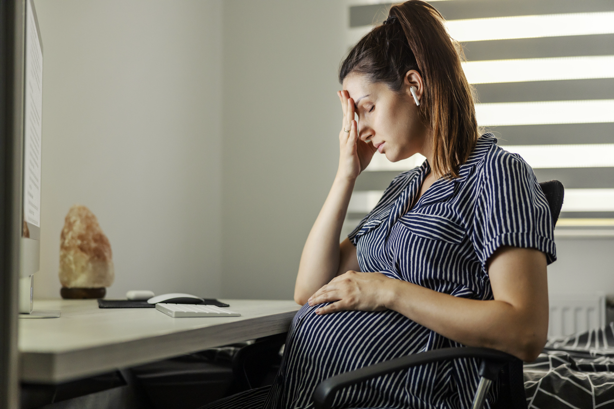 pregnant woman sitting at her desk with one hand on her forehead